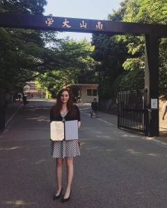 Kayla standing in front of Nanzan University with program completion certificate.